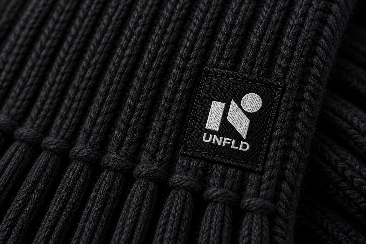 Black UNFLD woven label stitched onto charcoal knit